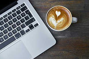 MacBook Pro beside white ceramic mug with espresso