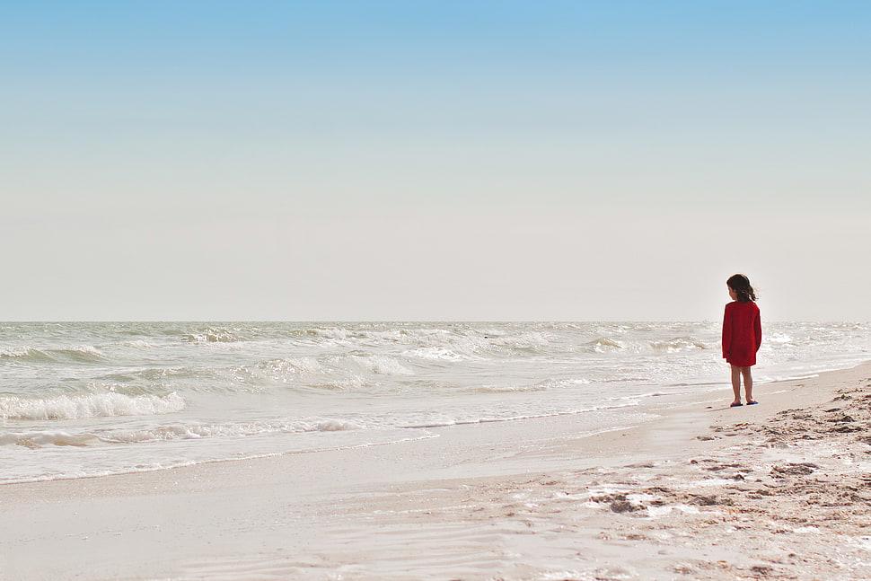 toddler girl wearing red dress standing on seashore during daytime HD wallpaper