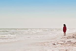 toddler girl wearing red dress standing on seashore during daytime