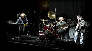 three men playing guitar, drums, and piano on stage