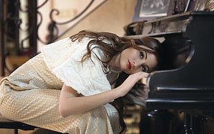 woman wearing white and beige dress sitting in front of black upright piano