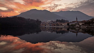 inline buildings mirrored on calm body of water in distance silhouette of mountain during golden hour
