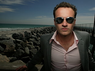 man in gray notch lapel suit jacket and black sunglasses near seashore HD wallpaper