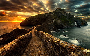 concrete pathway leading on hill with house surrounded by body of water