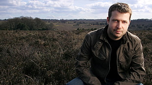 man in black zip-up jacket and blue denim pants surrounded by grass