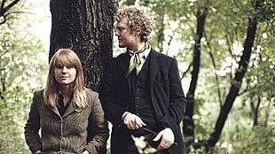 man wearing black suit standing beside woman in woods