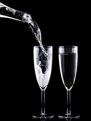 glass bottle pouring liquid on two clear glass champagne flutes