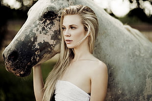 woman in white strapless top holding white and black horse near face