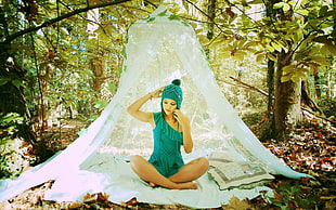 woman in teal romper sitting on white textile near trees