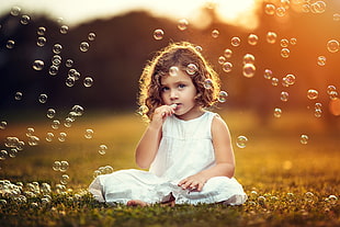 blonde haired girl sitting on green grasses surrounded with bubble