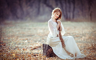 woman wearing white long-sleeved dress sitting on log