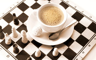 white ceramic cup with saucer on top of chessboard