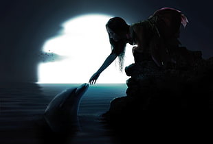 woman reaching dolphin in sea during night time