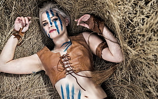 woman in brown leather lace-up sleeveless crop top lying on the grass with blue face art