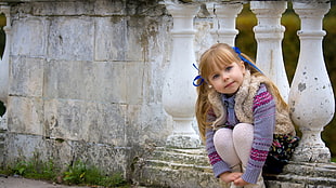 girl in purple sweater sitting in front of white concrete baluster