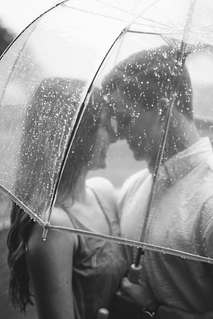 grayscale photography of couple under transparent umbrella on rainy day