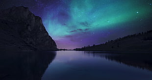 aurora borealis above the body of water beside the mountain