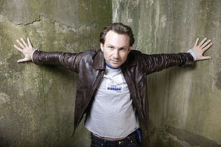 man wearing brown leather jacket standing beside a wall