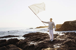 man wearing gray long-sleeve shirt holding white flag standing near ocean during daytime