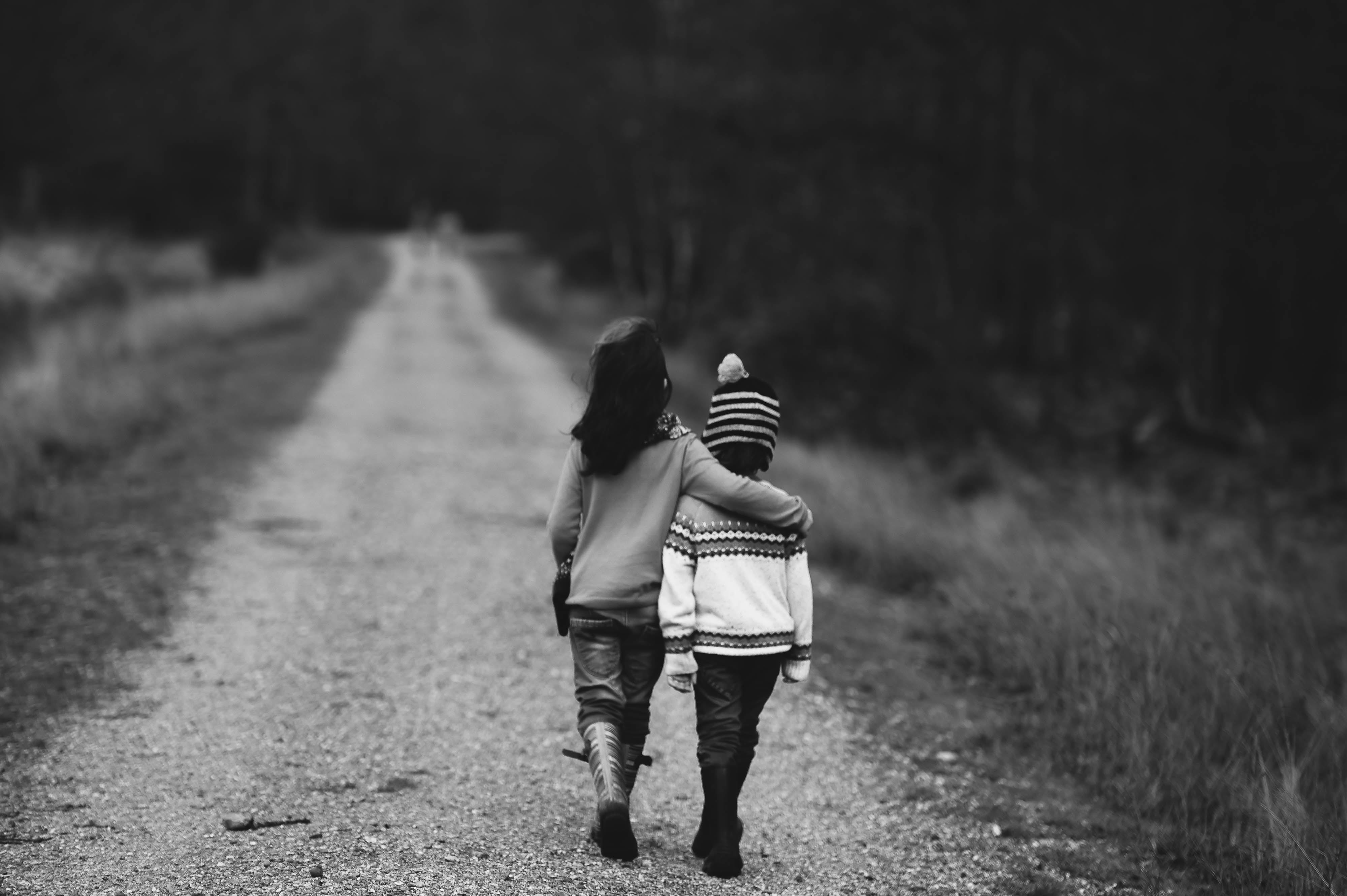 gray scale photo of two toddler walking on road