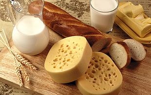 two sliced cheese on brown wooden plate with brown bread and a glass of milk