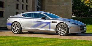 silver Aston Martin sedan on brown concrete road near building