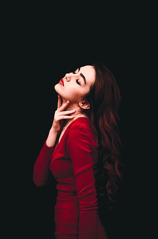 woman holding her neck while wearing red long sleeved dress against black background
