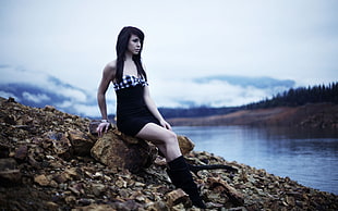 woman wearing black tube dress sitting on brown rock