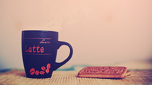 black and red Latte print ceramic mug with two biscuits on brown surface