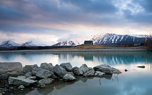 landscape photography of rocks on water near frosted mountain