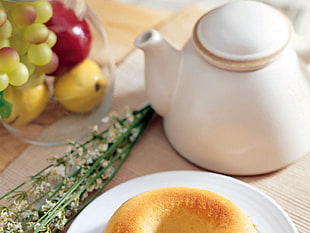 closeup photo of bread on saucer beside teapot and flower