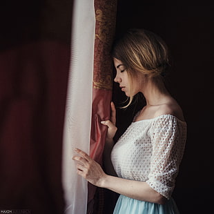 photography of woman in white blouse standing in front of window