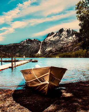 beached brown SLR boat raft near brown wooden pier and mountain range under clear sky during daytime HD wallpaper