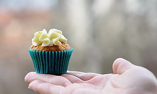 selective focus photography of chocolate cupcake with yellow topping on person's right palm