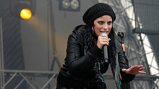 woman in black leather jacket and black beanie cap holding microphone on stage