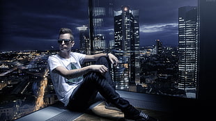 man in white shirt and black jeans sitting on rooftop at night time