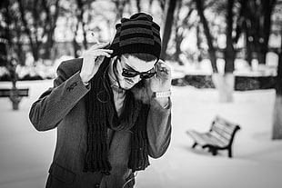 man wearing wayfarer sunglasses, scarf, knit cap and formal coat outfit in grayscale photography