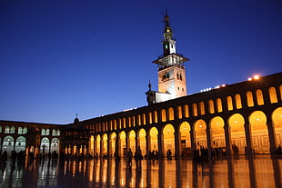 photo of orange lighted concrete building with people standing inside, damascus, umayyad mosque