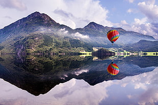 red and multicolored hot air balloon, lake, mountains