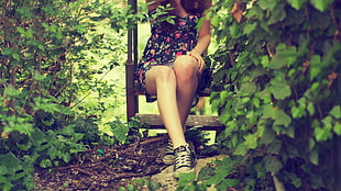 woman wearing black and pink floral dress sitting on bench surrounded by plants during daytime