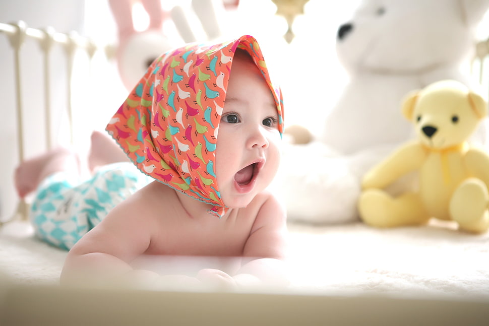 topless baby wearing orange, white, green and red birds print headband beside white and yellow bear plush toys HD wallpaper