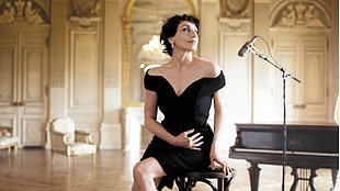woman wearing black sweetheart off-shoulder mini dress sitting on brown stool beside microphone and piano