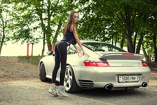 woman in blue tank top beside silver Porsche 911 Turbo S