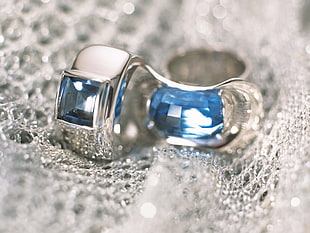 closeup photography of pair of silver-colored sapphire encrusted earrings