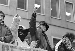 gray scale photograph of man in coat raising his hand