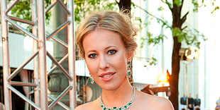 selective focus photo of blonde woman wearing emerald encrusted silver-colored bib necklace
