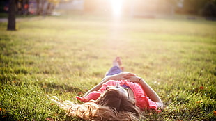selective focus photography of woman in pink shirt lying on green grass