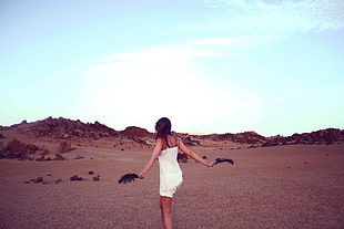 woman wearing white sleeveless dress standing on brown sands