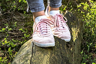 person wearing pink low-top shoes stepping on brown wooden trunk at daytime