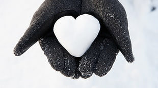 person in black winter gloves holding snow in heart shape